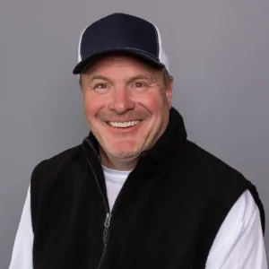 man smiling, wearing black vest and black hat
