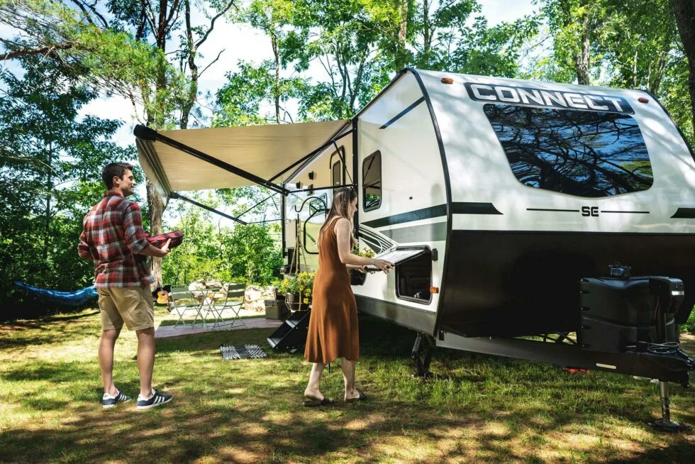 A man and woman setting up their campground outside of their RV, in warm weather.