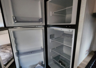 A photo of an open refrigerator with four compartments. The top two compartments are freezer sections, each with a single shelf. The bottom two are fridge sections with multiple shelves and a drawer. Shelves and compartments are empty.