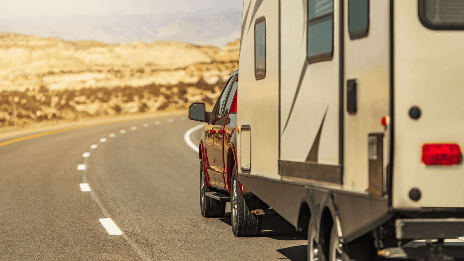 PPRV Blog Featured Images A red pickup truck tows a beige RV from one of the Best Travel Trailer Brands along a winding highway through a dry, desert landscape with sandy hills under a partly cloudy sky.