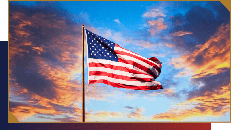 An American flag waves on a flagpole against a vibrant sky with colorful clouds at sunrise or sunset.